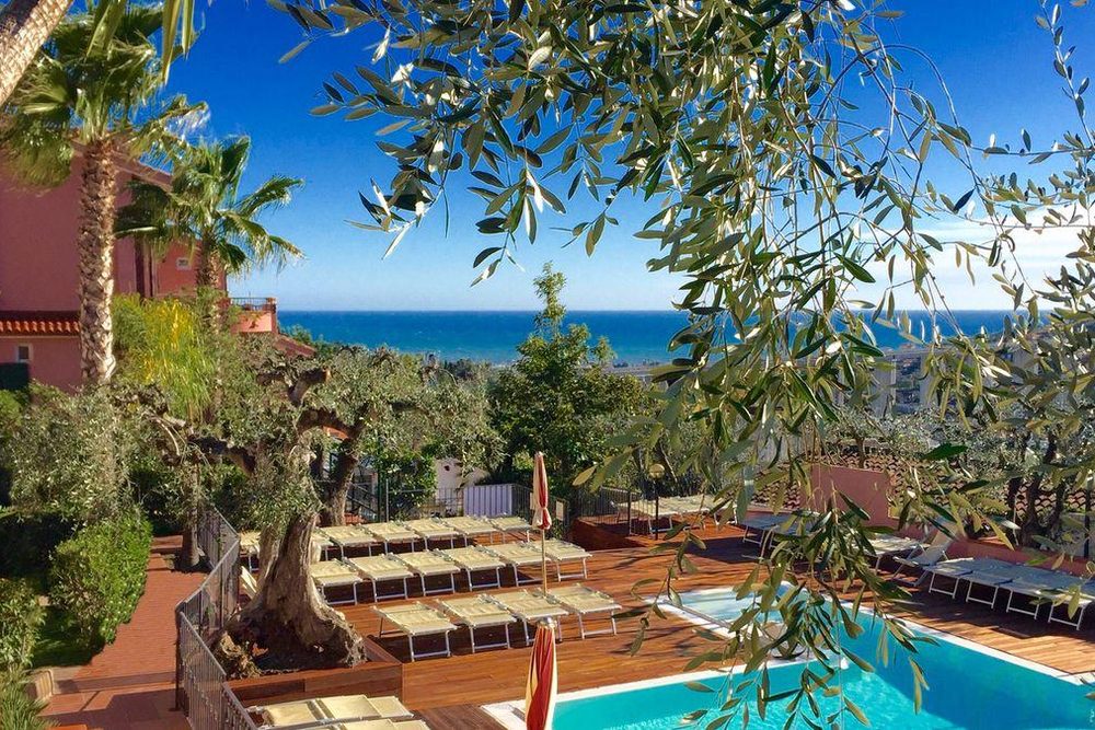 La piscine de l’hôtel Villa Giada Resort sous les oliviers, les transats au bord de l’eau et la mer en contrebas.