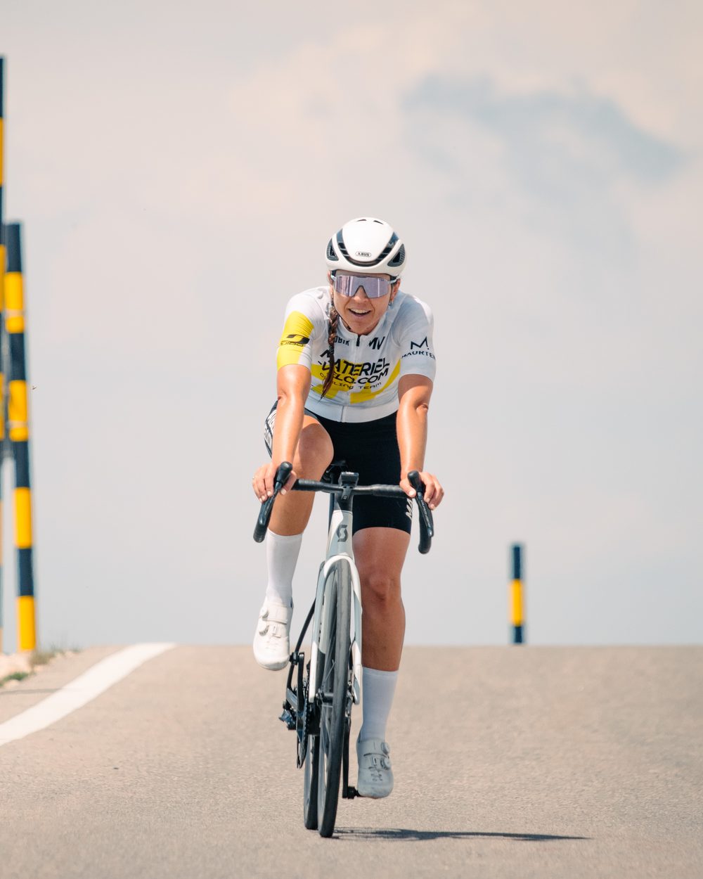 Une cycliste en maillot Materiel-velo.com monte le mont Ventoux, les bornes noires et jaunes derrière elle.