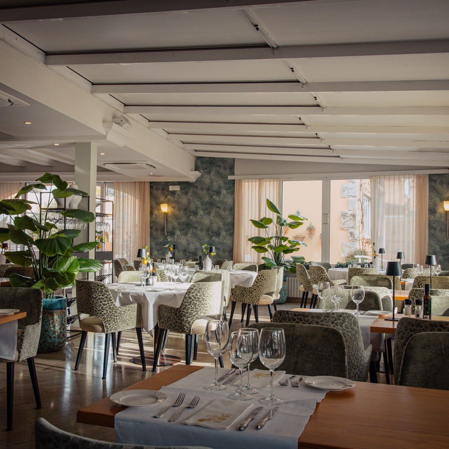 La salle à manger de l’hôtel, des tables dressées de nappes blanches, des plantes vertes et de grandes fenêtres.